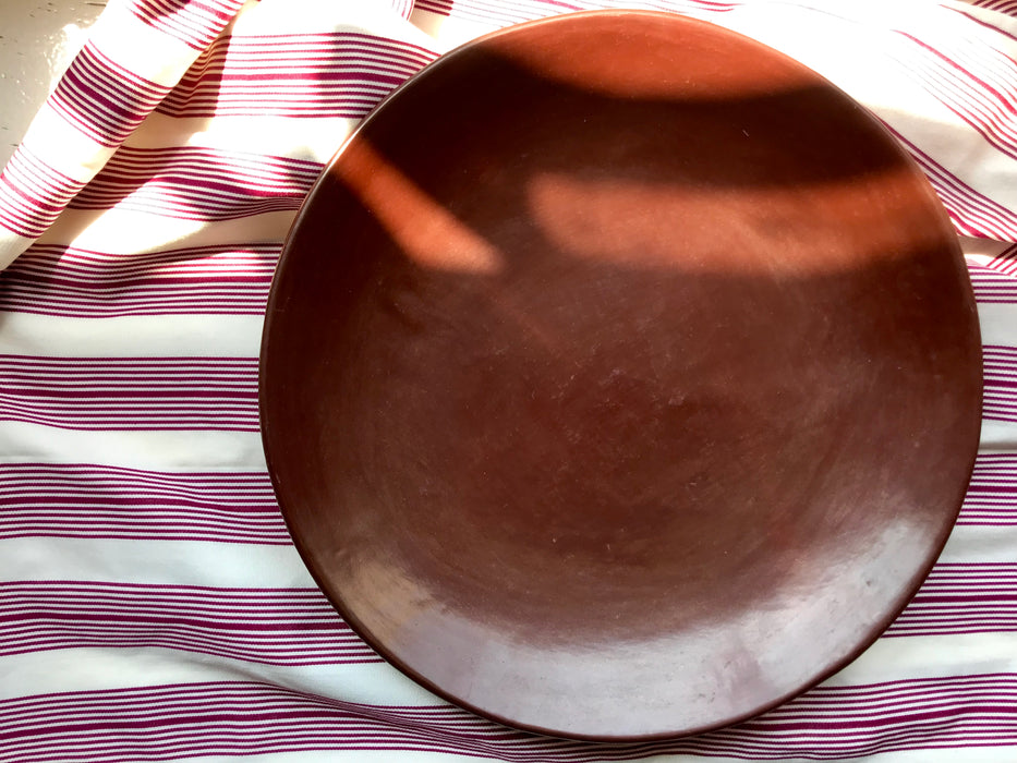 Mexico 1492: Brown serving plate, hand made out of humble clay, then burnished with a piece of quartz to shine. This plate reflects the warmth of the Earth and the modest origins, brought to the spotlight by caring artisan's hands.   Dimensions: D 34cm (13.5”)