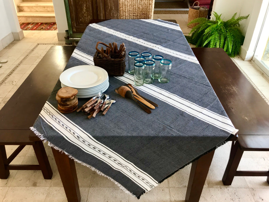 Mexico 1492: Pure cotton tablecloths with 4 stripes and braids, handmade on a pedal loom, by tenured, skillful artisans in one of the oldest, family-owned weaving workshops in Patzcuaro, Michoacan.   Available in 4 color combinations: Charcoal, Charcoal & Pebble, Pitaya & Grape and Oaxaca Sand. Each comes with 8 matching napkins.  L 2m (78.7") x W 2m (78.7")