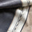 Mexico 1492: Pure cotton charcoal & pebble-colored tablecloth with 4 stripes and braids, handmade on a pedal loom, by tenured, skillful artisans in one of the oldest, family-owned weaving workshops in Patzcuaro, Michoacan.   Available in 4 color combinations: Charcoal, Charcoal & Pebble, Pitaya & Grape and Oaxaca Sand.  L 2m (78.7") x W 2m (78.7")