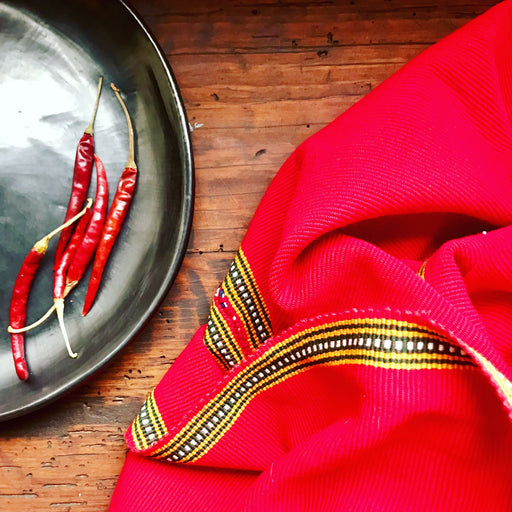 Mexico 1492 - bright red table cloth with colorful edges, handmade on a backstrap loom in Chiapas Mexico. Paired with Black Clay plate from the same shop. 